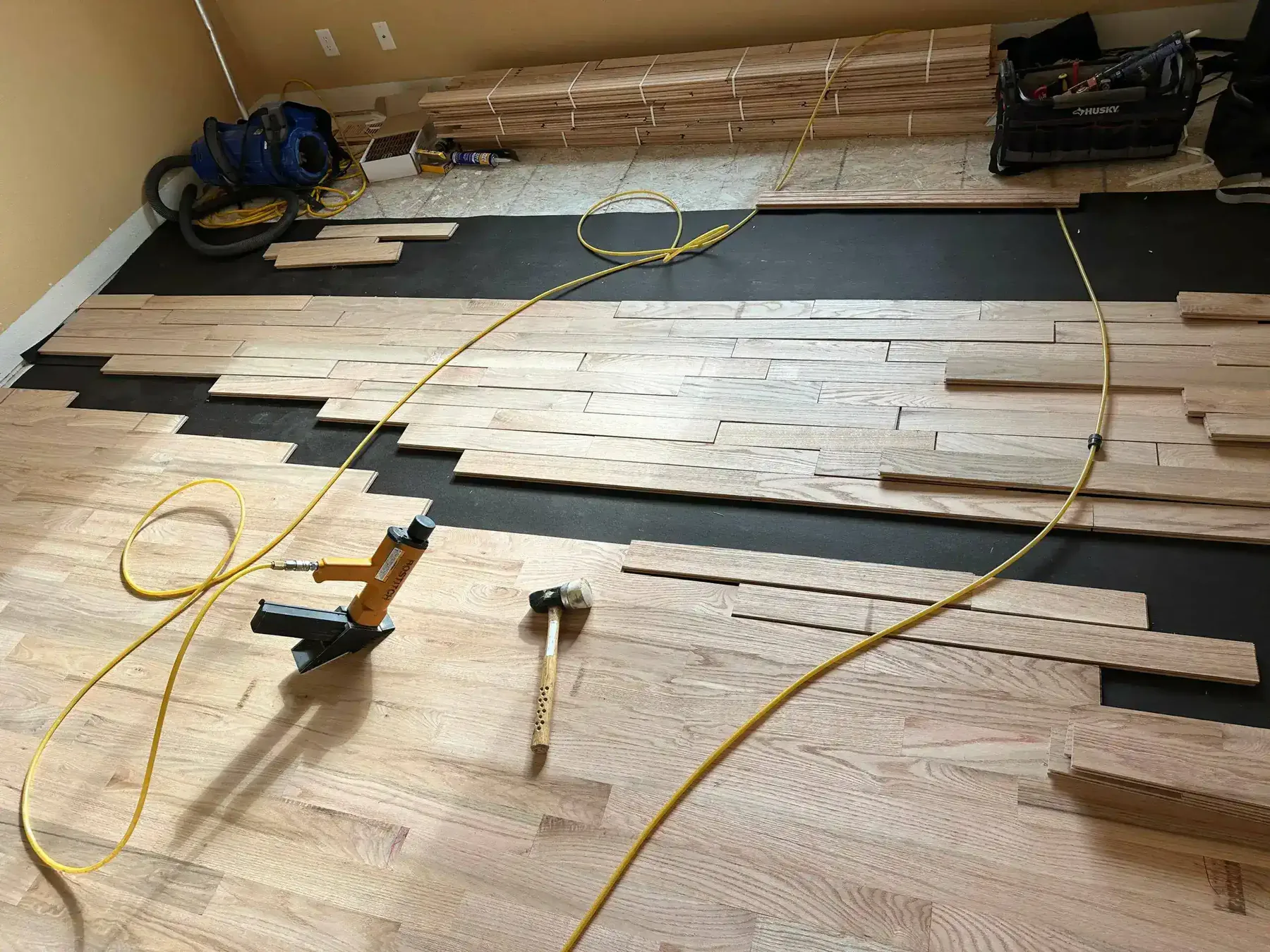 Unfinished solid hardwood boards being nailed down over black underlayment