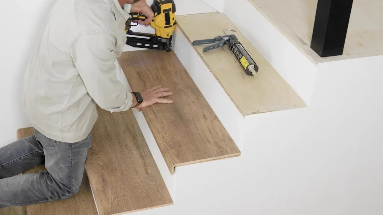 Installer fitting a wood-look tread onto a staircase with a nail gun