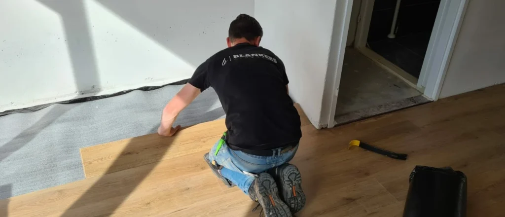 Installer laying wood-look vinyl plank over grey underlay