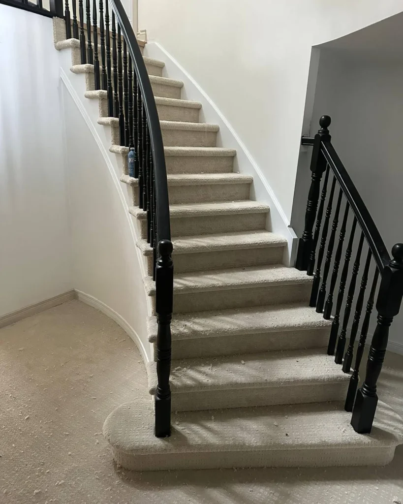 Curved staircase with new beige carpet wrapped over each tread and a black iron railing