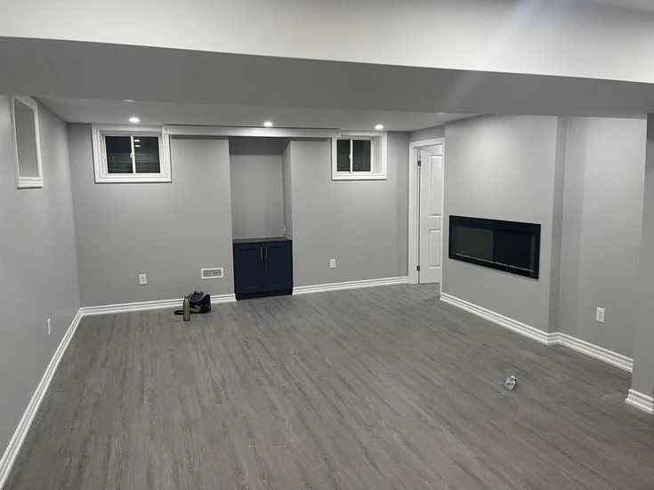 Finished basement with grey vinyl plank, white baseboards and a wall fireplace
