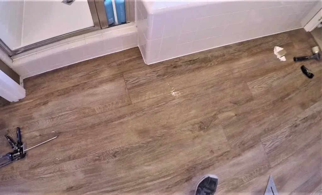 Brown wood-look vinyl plank laid in a bathroom up to the tub, with tools still on the floor