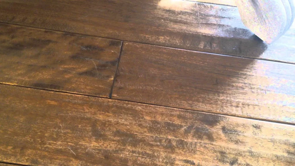 Worn finish on brown hardwood planks being coated with a pad applicator