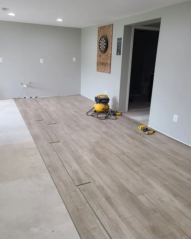 Light vinyl plank being laid across a levelled basement slab