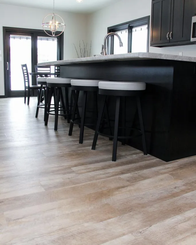 Light wood-look vinyl plank through a kitchen with a black island and bar stools