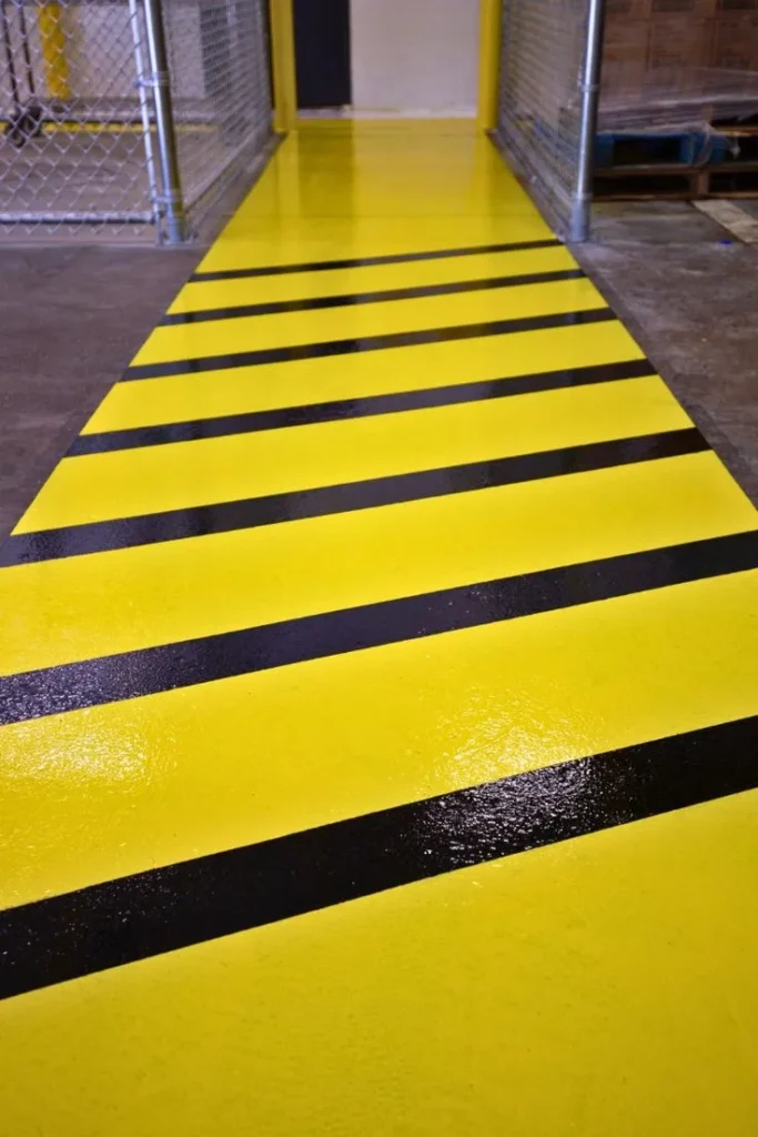 Yellow safety floor coating with black diagonal stripes along a warehouse walkway
