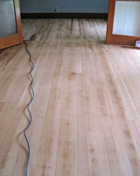 Strip hardwood sanded back to bare wood, with the sander cord running across the floor